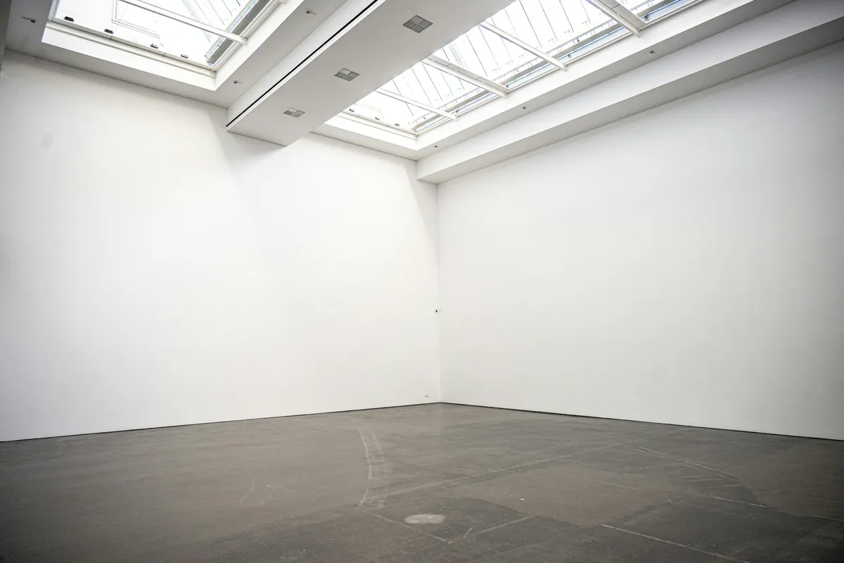Empty white-plaster gallery room with skylights flooding cool light across the concrete floor