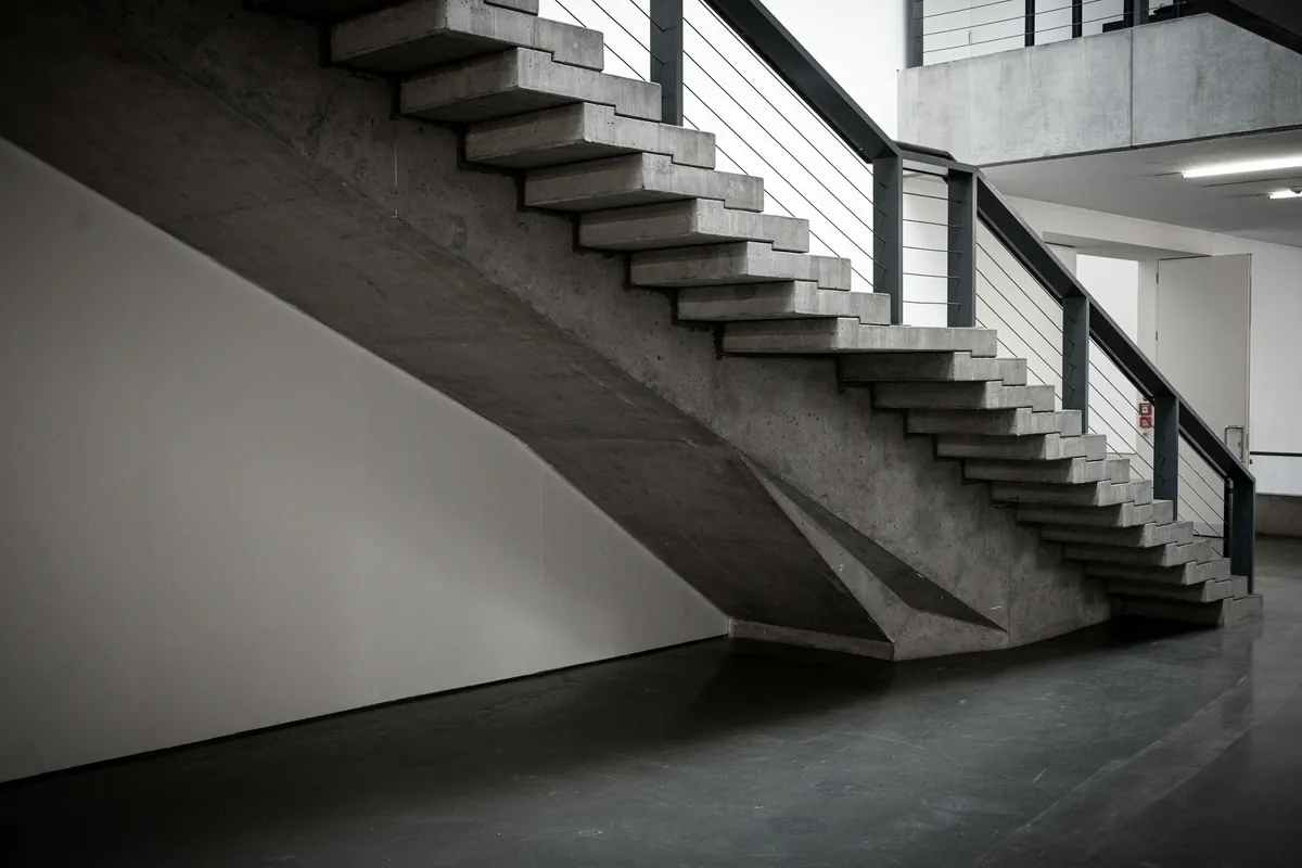 Concrete staircase with steel railing alongside white plaster wall, geometric shadow paired with structure