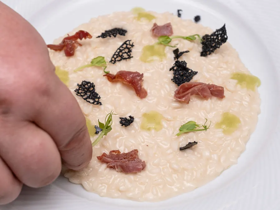Chef decorating risotto with black truffle and prosciutto
