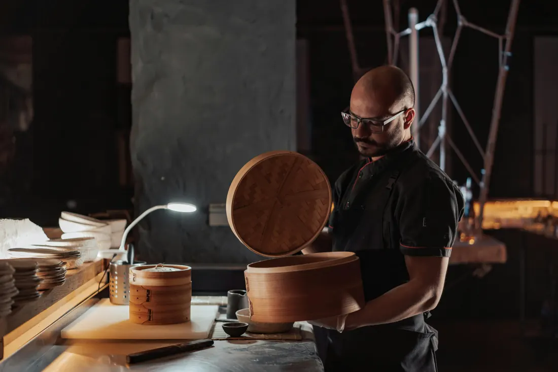 Chef opening a bamboo steamer in a professional kitchen