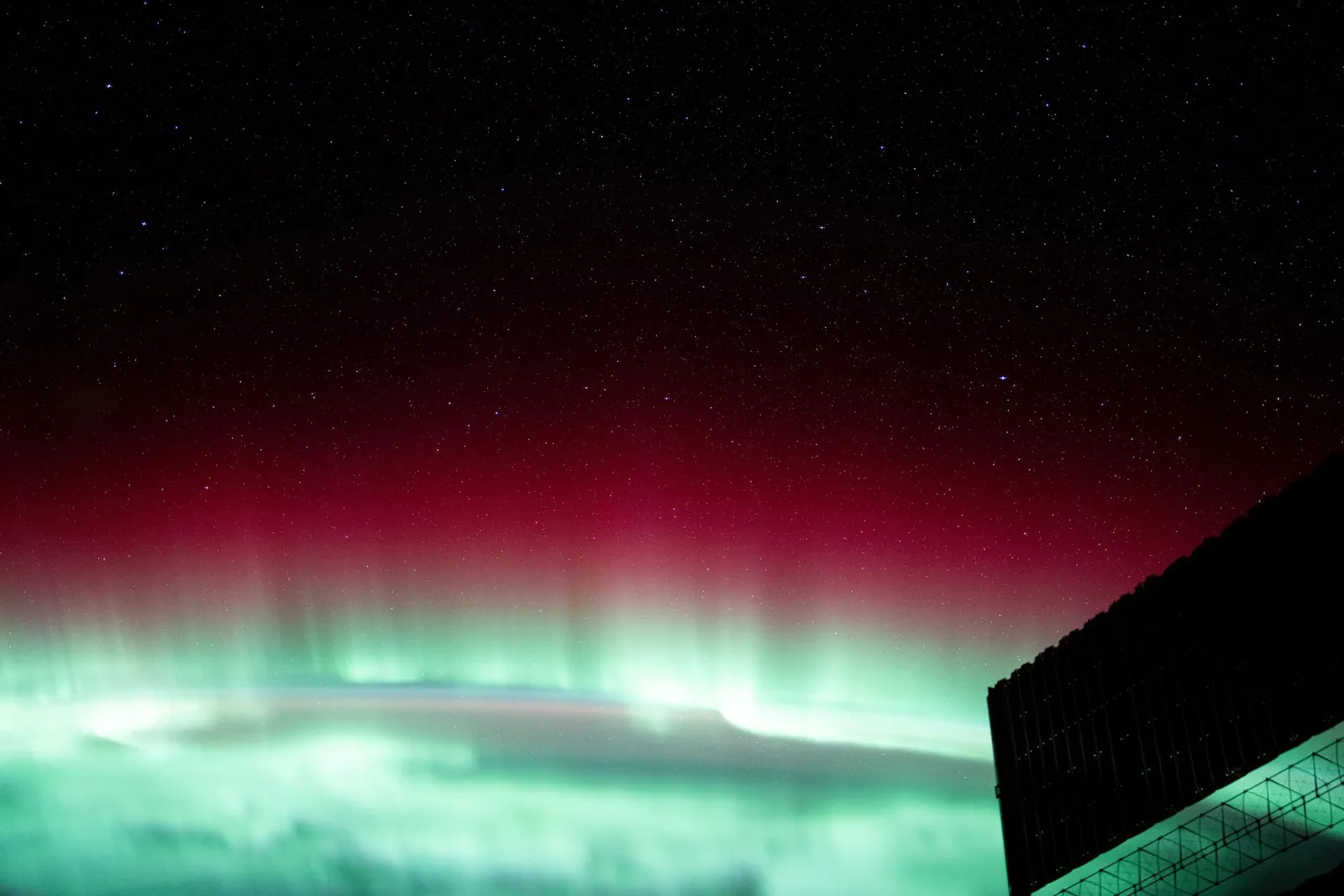 An aurora seen from orbit, green light folding over the night side of the Earth.